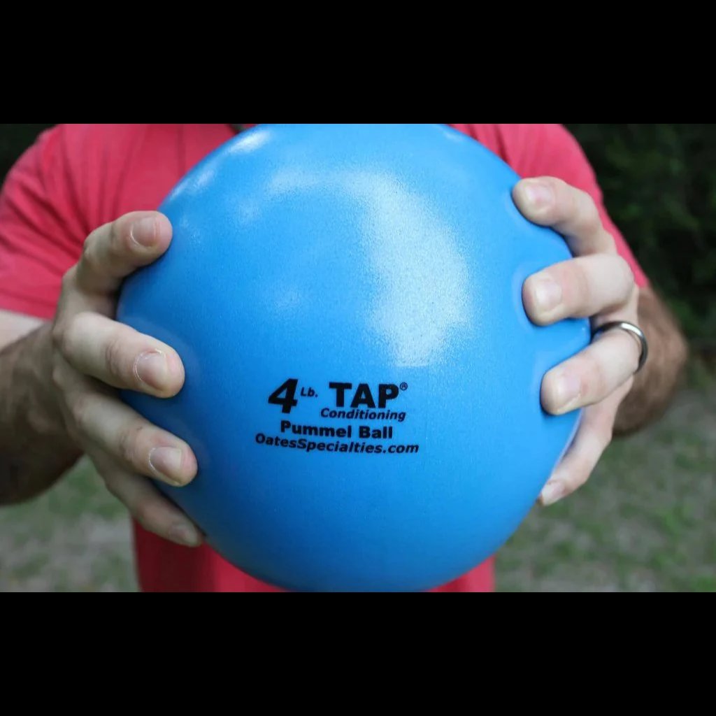 An athlete grips a blue 4lb pummel ball with two hands showing the size and the textured finish.
