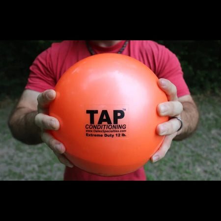An athlete grips a orange 12lb pummel ball with two hands showing the size and finish.