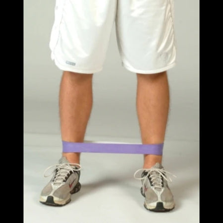 Athlete walking laterally with a resistance band looped around the ankles, emphasizing hip abductor and adductor activation during controlled side steps.