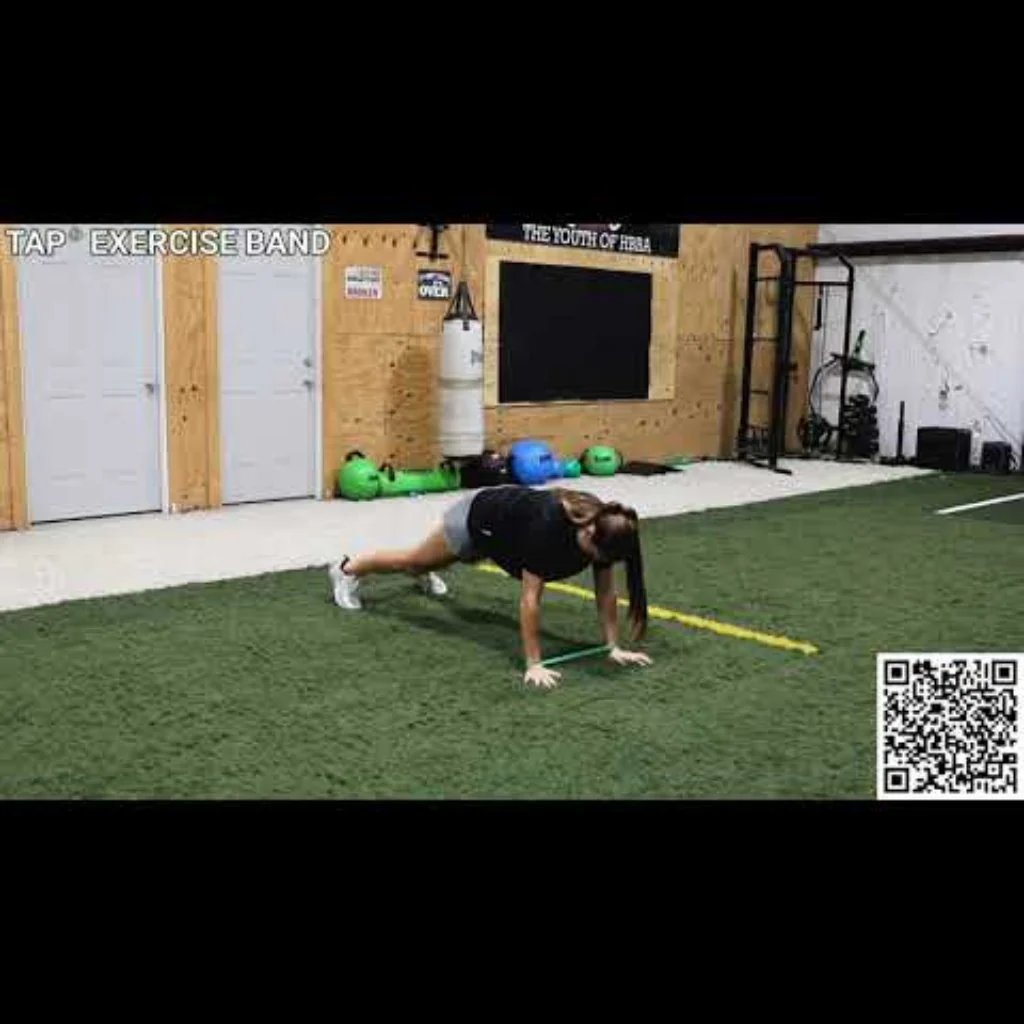 Athlete performing lateral movements in a training facility with a resistance band looped around the wrists, emphasizing upper body activation, shoulder stability, and dynamic control.