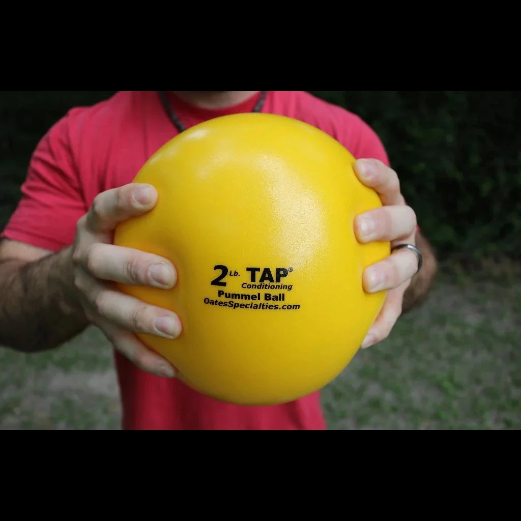 An athlete grips a yellow 2lb pummel ball with two hands to display the size of the size and textured finish of the optimized 2lb ball for explosive movement pattern training.
