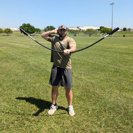 An athlete holds the TAP® Shoulder Tube in front of him, moving it up and down with palms facing downward to create a dynamic wave-like motion. This action engages the shoulder scapulae and activates the front deltoid for targeted muscle activation.