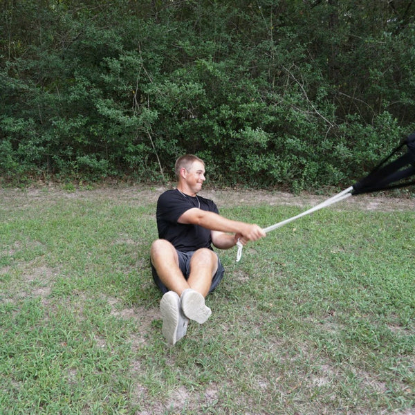 Person performing seated side-to-side slam exercises with TAP® Hammer Net outdoors - core and oblique strengthening workout demonstration for athletic improvement and durability.