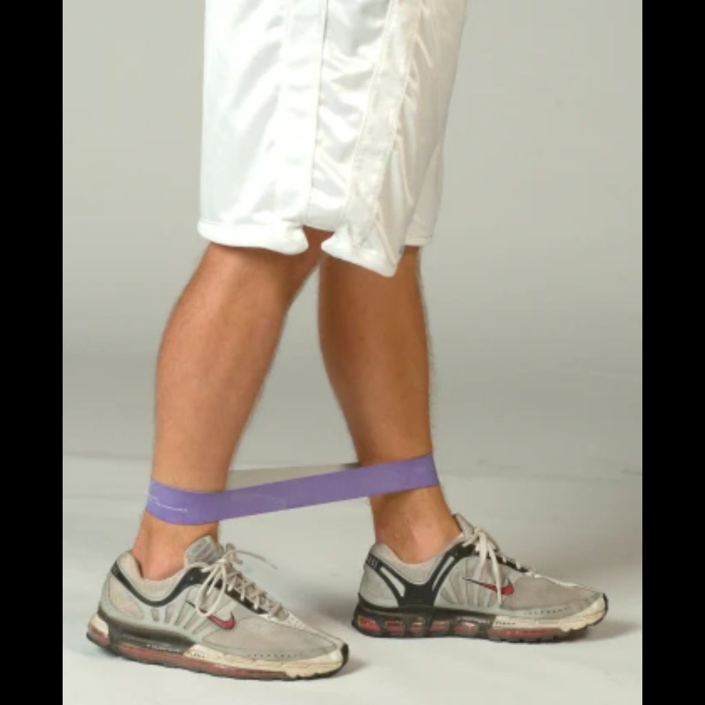Athlete performing resisted walking with a resistance band looped around the ankles, emphasizing targeted activation of hip abductors and adductors during lateral movement.