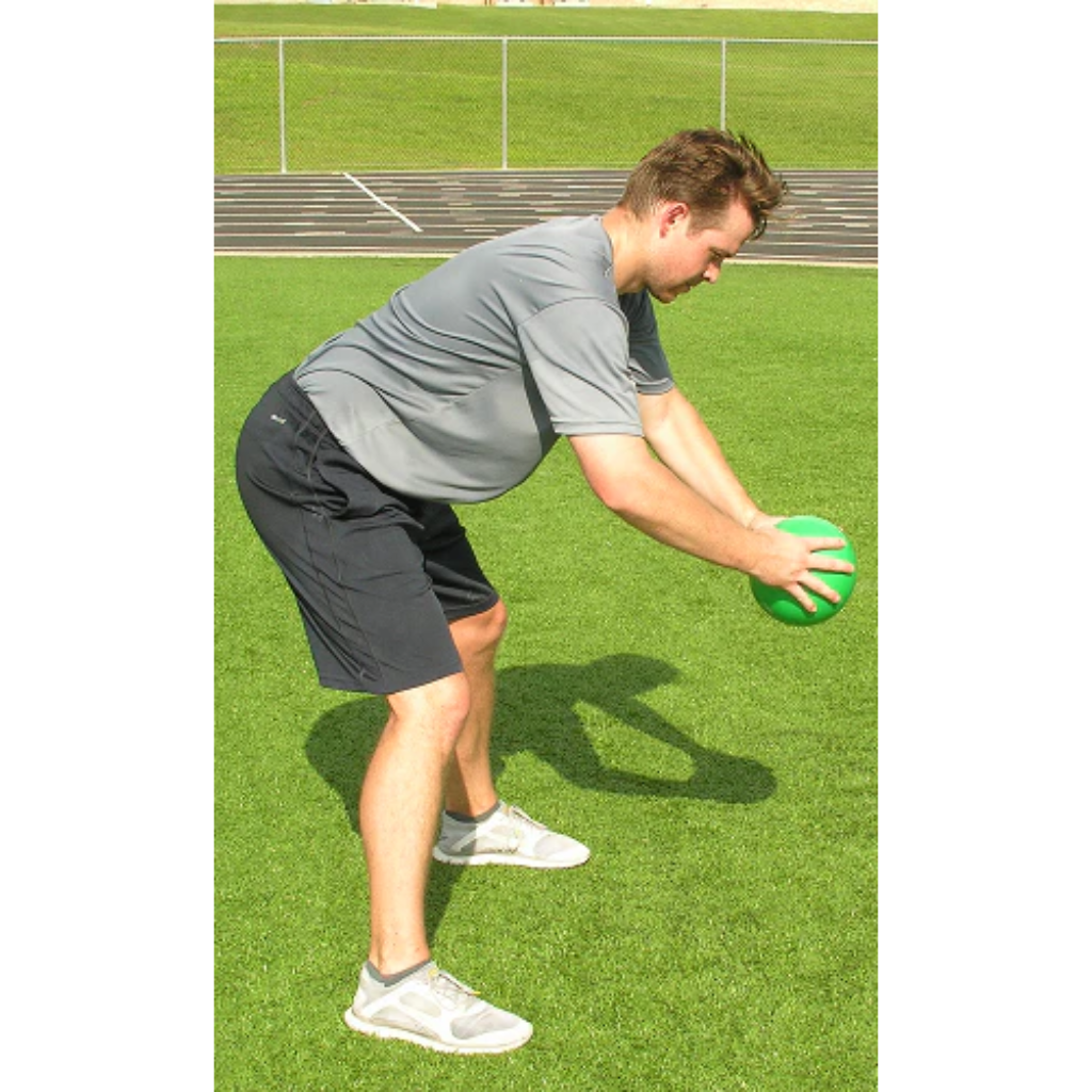 Athlete holding a green pummel ball at knee level, just before releasing it for a ground slam.