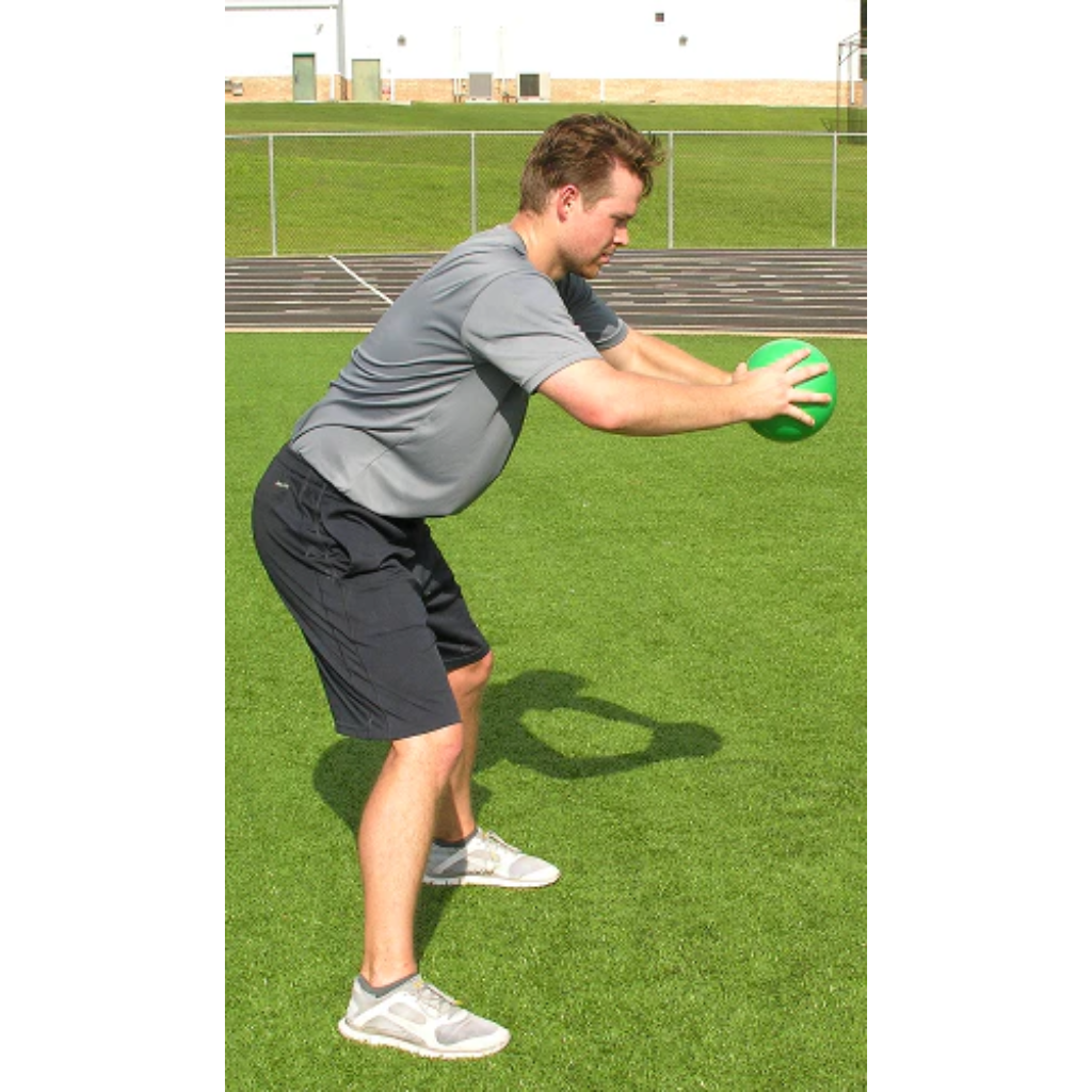 Athlete leans over, holding a green pummel ball with both hands in a side profile view.