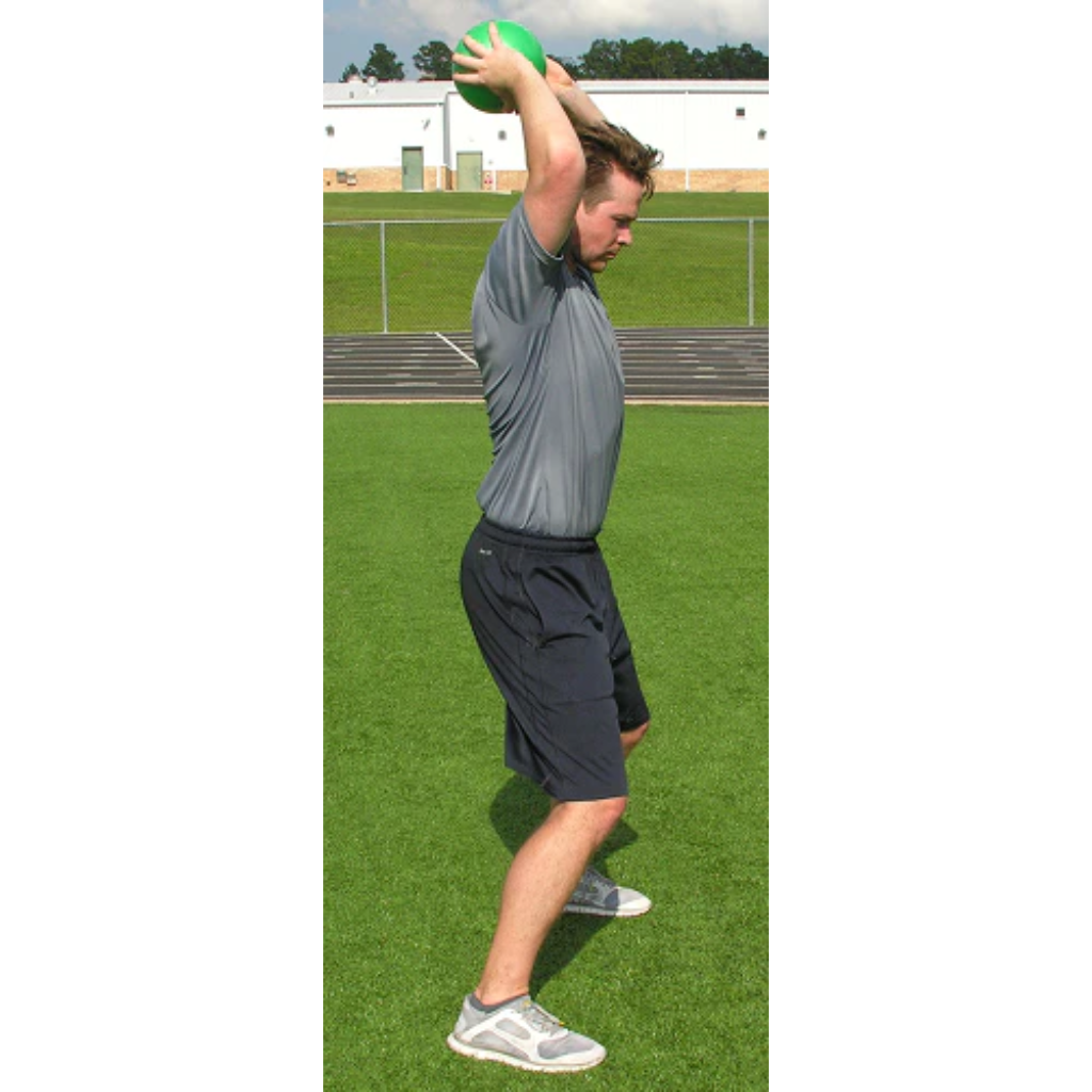 Athlete in a side profile holds a green pummel ball with both hands raised overhead, preparing for a slam.