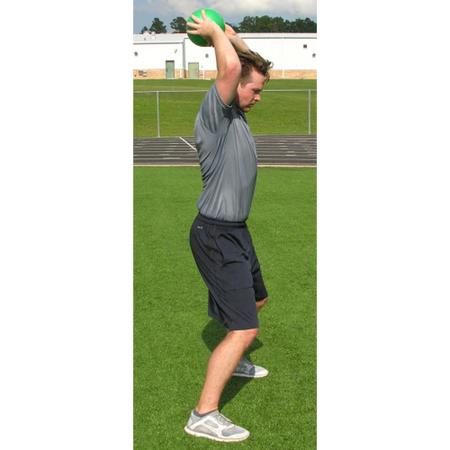 Athlete in a side profile holds a green pummel ball with both hands raised overhead, preparing for a slam.
