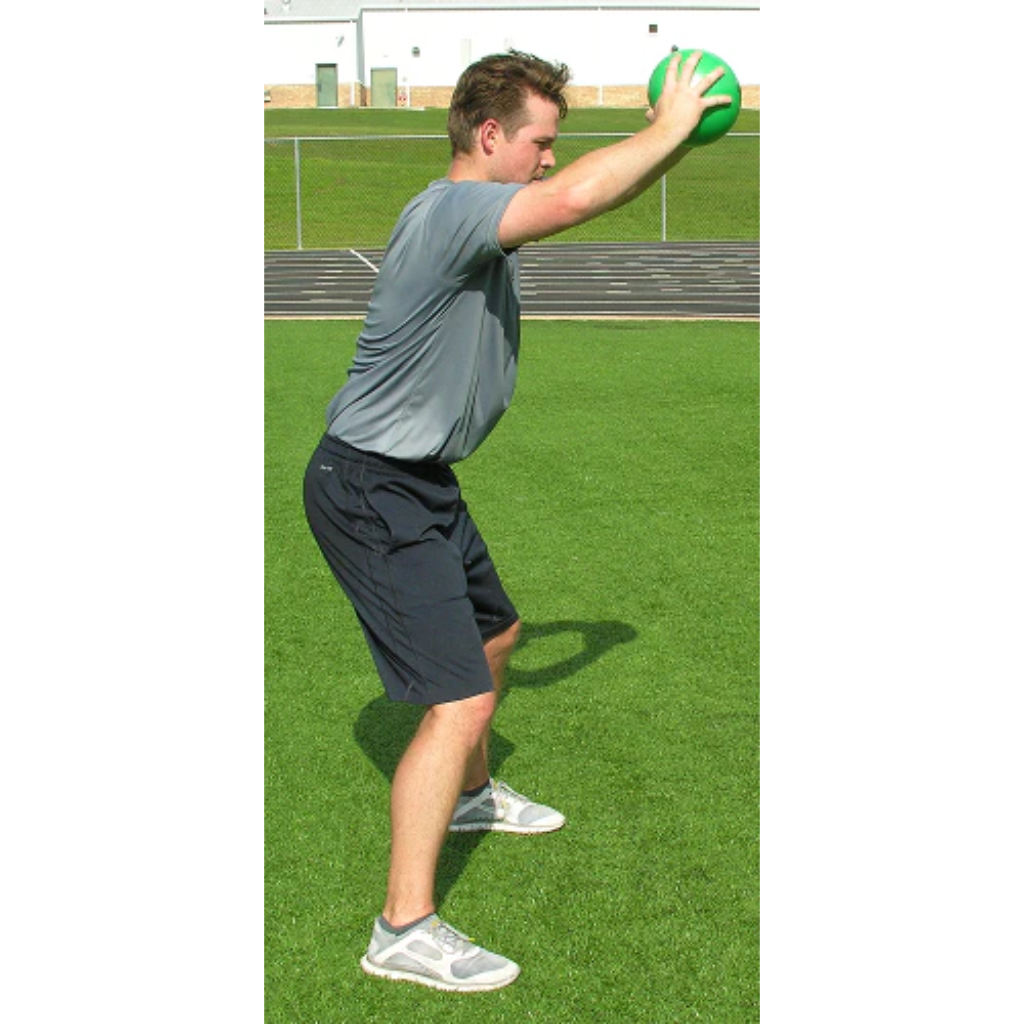 Athlete gripping a green pummel ball at eye level with both hands, slamming it to the ground.