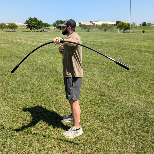 An athlete grips the TAP® Shoulder Tube with palms facing down, moving it vertically to generate oscillations. The controlled resistance engages and strengthens the arm and shoulder complex, making it an effective dynamic warm-up tool.