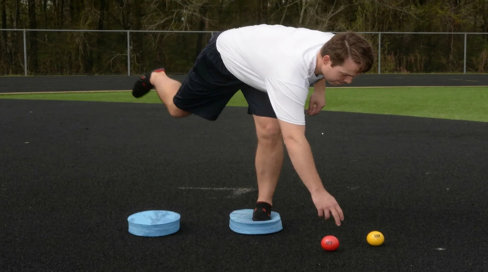 Athlete maintaining ankle stability on an Oval Balance Pad while reaching for a red ball, demonstrating balance, coordination, and controlled movement during training.