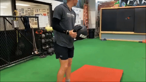 Baseball pitcher shaking a KHAOS® Water Ball to activate core muscles and enhance body stabilization before simulating a pitching delivery, optimizing dynamic control and strength.