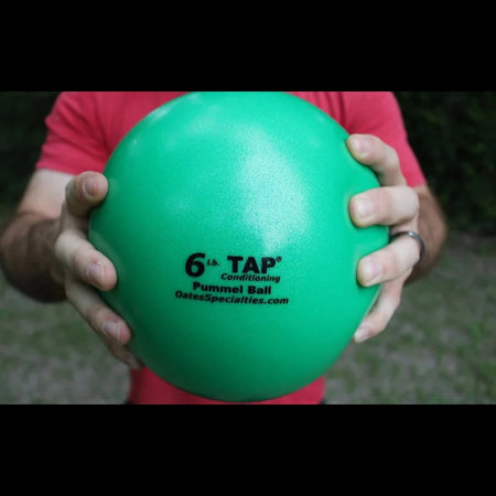 An athlete grips a green 6lb pummel ball with two hands showing the size and the textured finish.