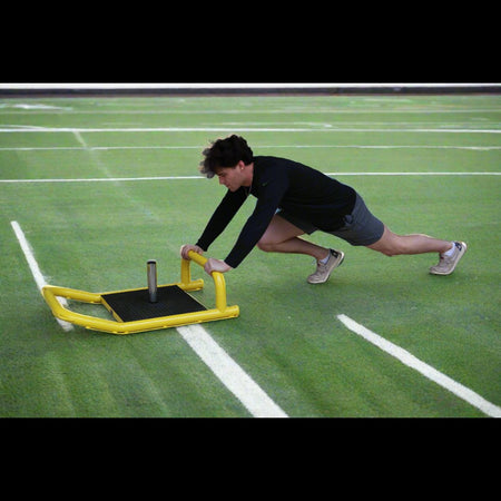 Athlete pushing resistance sled on turf for lower body power and strength training.