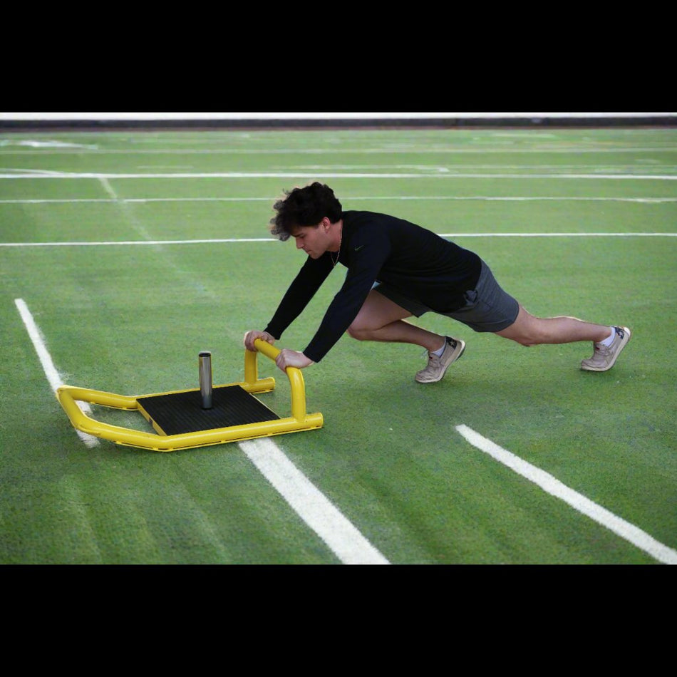 Athlete pushing resistance sled on turf for lower body power and strength training.