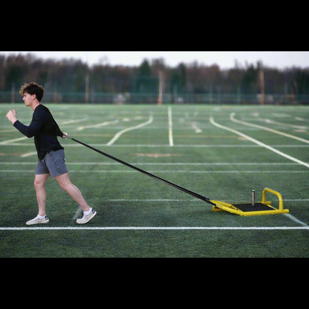 Athlete pulling resistance sled across turf using included tow strap attached to body for strength and conditioning.