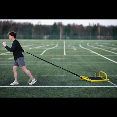 Athlete pulling resistance sled across turf using included tow strap attached to body for strength and conditioning.