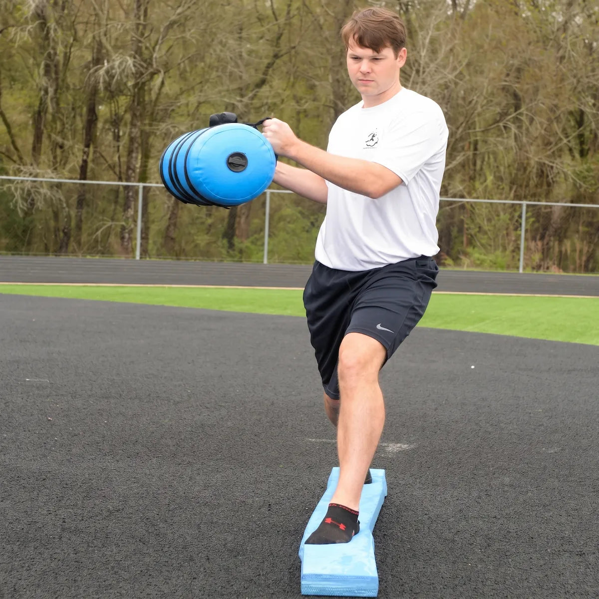 Athlete performing a lunge and trunk twist with a Blue Waterboy on the Folding Balance Beam, utilizing compounded unstable variable stimuli for lead-side stabilization and kinetic chain organization.