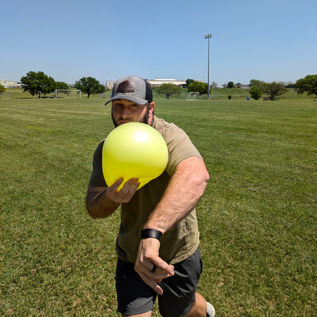 An athlete grasps the TAP® Connection Ball in the glove side hand. The athlete has released the baseball, and the body has rotated to the glove side with the Connection Ball. The Connection Ball is on the athlete's cheek symbolizing efficient glove side patterns.