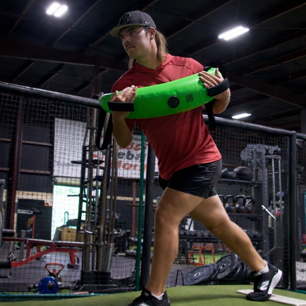 Side view of an athlete holding the Khaos® Bulgarian Water Bag against their chest during rotational core training. The dynamic water movement challenges stabilization, crucial for baseball pitching power and accuracy.