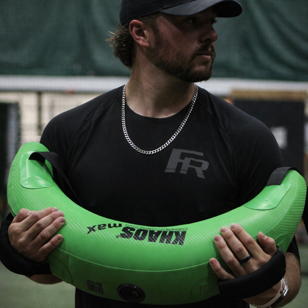 Pitcher holding the Bulgarian Water Bag against his chest, preparing to execute a rotational drill that engages core stability, strength, and dynamic movement control.