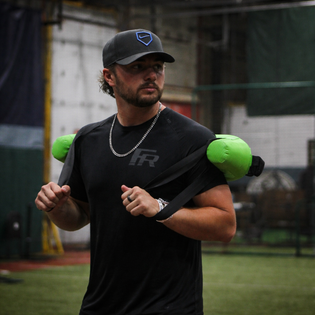 Pitcher from the front performing a pitching delivery with a Bulgarian Water Bag draped over his shoulders, utilizing shifting water resistance to enhance core stability, strength, and dynamic movement control.