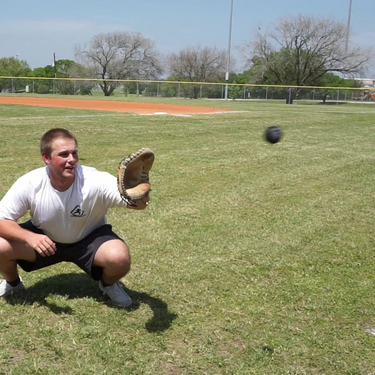 Catcher receiving a pitch with a DTS weighted training ball, utilizing a variable-load stimulus to drive scapular stabilization and kinetic chain organization for increased power in the throwing arm.