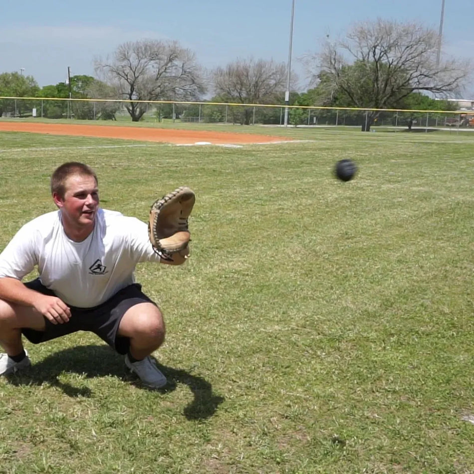 Catcher receiving a pitch with a DTS weighted training ball, utilizing a variable-load stimulus to drive scapular stabilization and kinetic chain organization for increased power in the throwing arm.