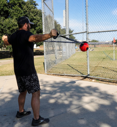 Athlete performing a standing lateral pull combining the sheathed tubing and Shoulder Shaker to drive scapular stabilization and kinetic chain organization via compound rhythmic perturbations.