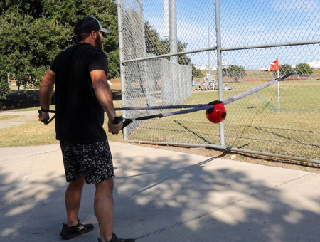 Athlete performing a standing rear row combining the sheathed tubing and Shoulder Shaker to drive scapular stabilization and kinetic chain organization via compound rhythmic perturbations.