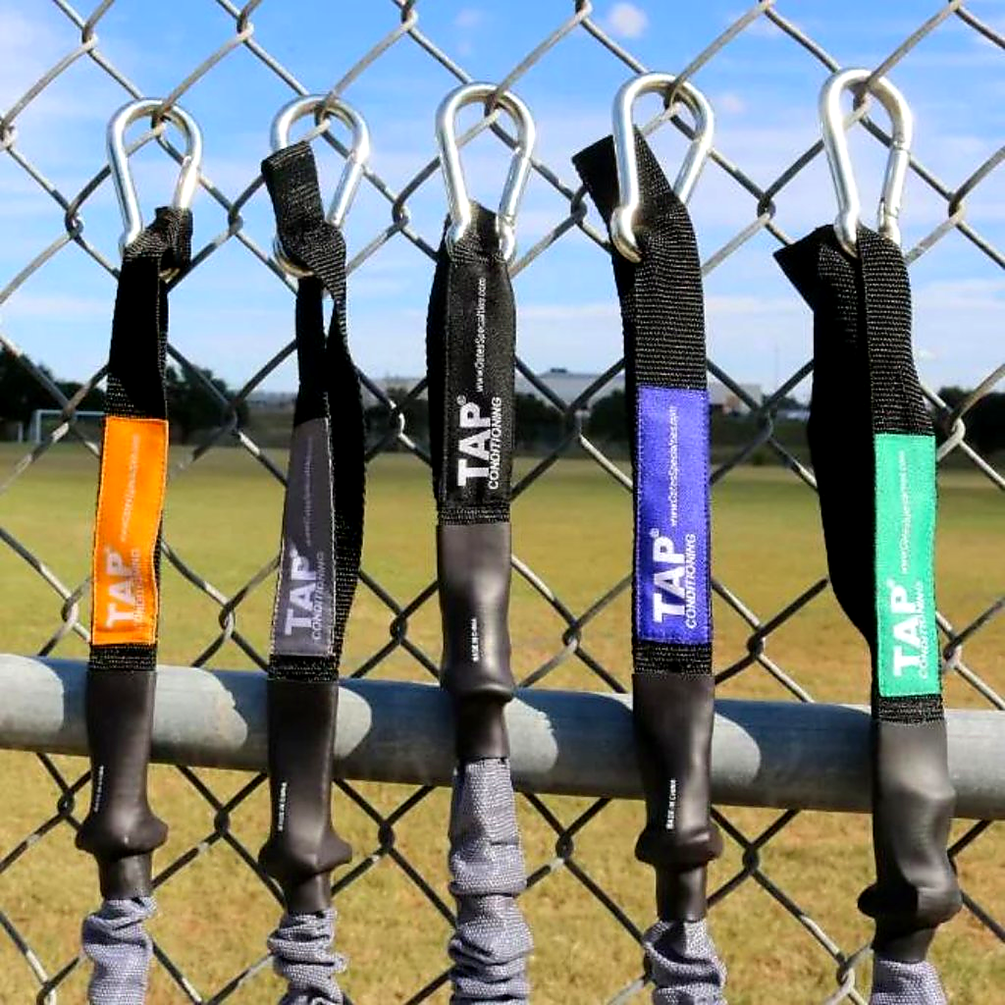 The complete developmental lineup of TAP® Sheathed Safety Tubing, showcasing the resistance hierarchy from Green to Gold. Each pair features a protective fabric sleeve that serves as a mechanical safeguard and elastic stop. The progression includes: Green (Youth), Blue (Junior High), Black (High School Standard), Silver (Collegiate), and Gold (Professional/Advanced). This system provides consistent neuromuscular feedback across the entire spectrum of Long-Term Athletic Development (LTAD).