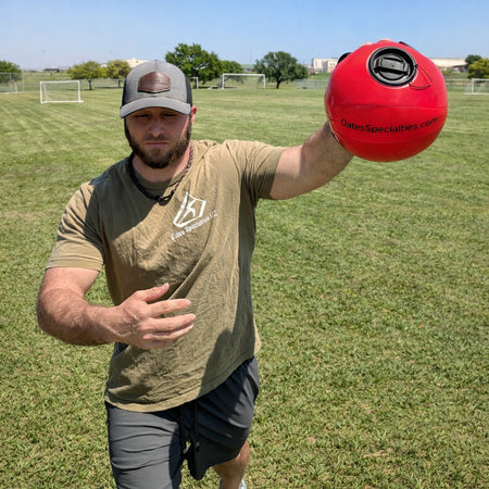 Athlete demonstrating the KHAOS® Shoulder Shaker in a pitching‑style motion, using unstable water resistance to train dynamic shoulder and scapular stability as part of a coach‑directed arm care routine