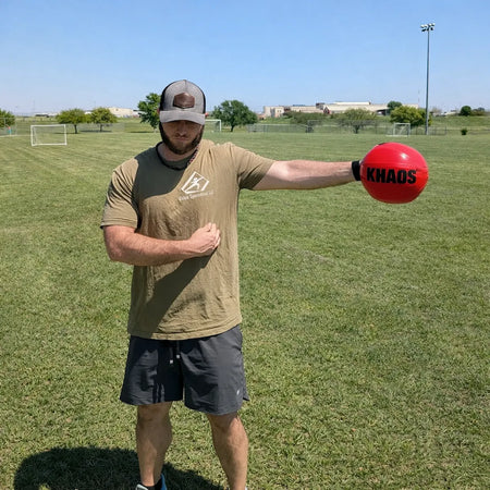 Athlete holding a KHAOS® Shoulder Shaker at their side during a dynamic pre‑throw warm‑up, using water‑turbulence perturbations to activate shoulder and scapular stabilizers for throwing‑arm preparation