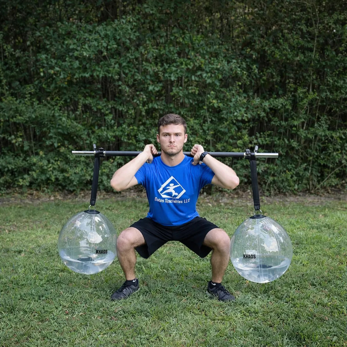Athlete performing a front rack squat with the KHAOS® Yoke, utilizing suspended water balls to drive anterior-load stabilization and maximize force transmission through the throwing chain.