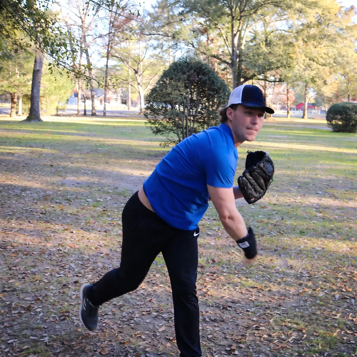 Baseball pitcher in the deceleration phase of a throw wearing the TAP® Weighted Forearm Sleeve, showing how the 16-ounce distal load engages the posterior shoulder and rotator cuff through the finish.