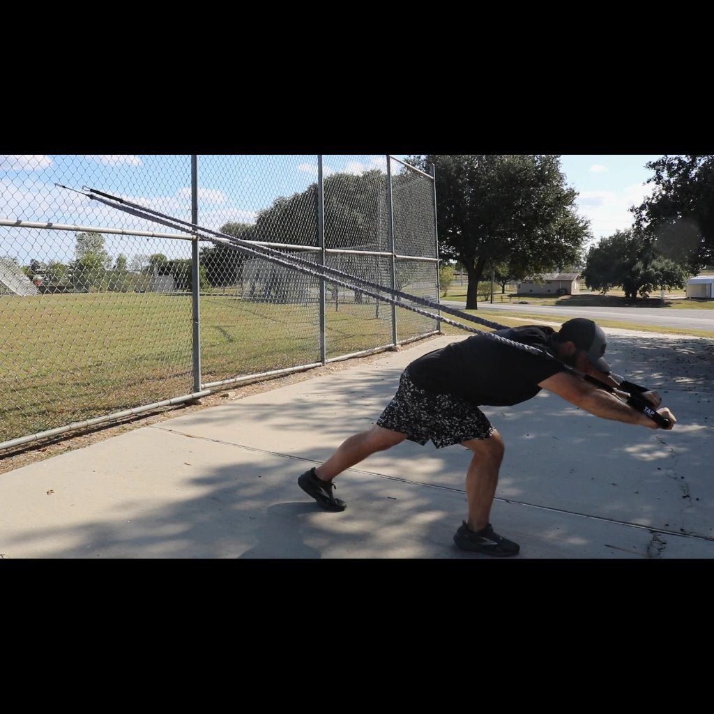 Athlete performing a full body exercise with TAP Sheathed Safety Tubing anchored to a fence. He is at full extension with a huge emphasis in core stability and strength.