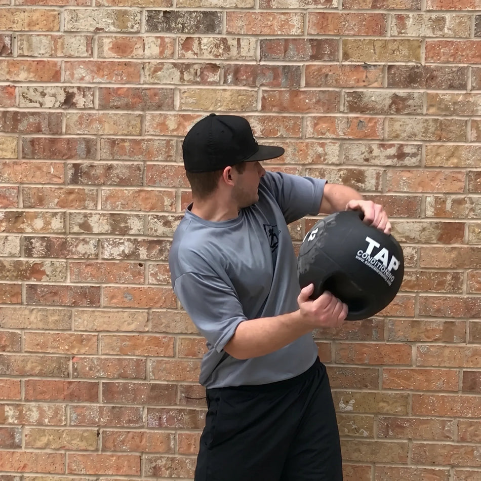 Athlete using a 12 lb Double Handle Medicine Ball against a brick wall—engaging in rotational strength training to enhance core power and functional movement.