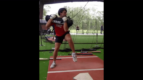 An athlete is cradling the KHAOS Waterboy (a bag filled with air and water) in front of his chest from shoulder to shoulder. His is acting like he is hitting, and going through a swing while stopping after the point of contact. This forces him to stabilize and self organize appropriately so he doesn't fall down.