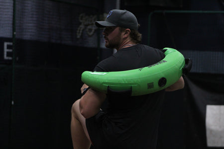Pitcher performing a pitching delivery with a Bulgarian Water Bag draped over his shoulders, utilizing shifting water resistance to enhance core stability, strength, and dynamic movement control.