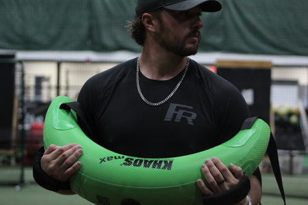 Pitcher holding the Bulgarian Water Bag against his chest, preparing to execute a rotational drill that engages core stability, strength, and dynamic movement control.