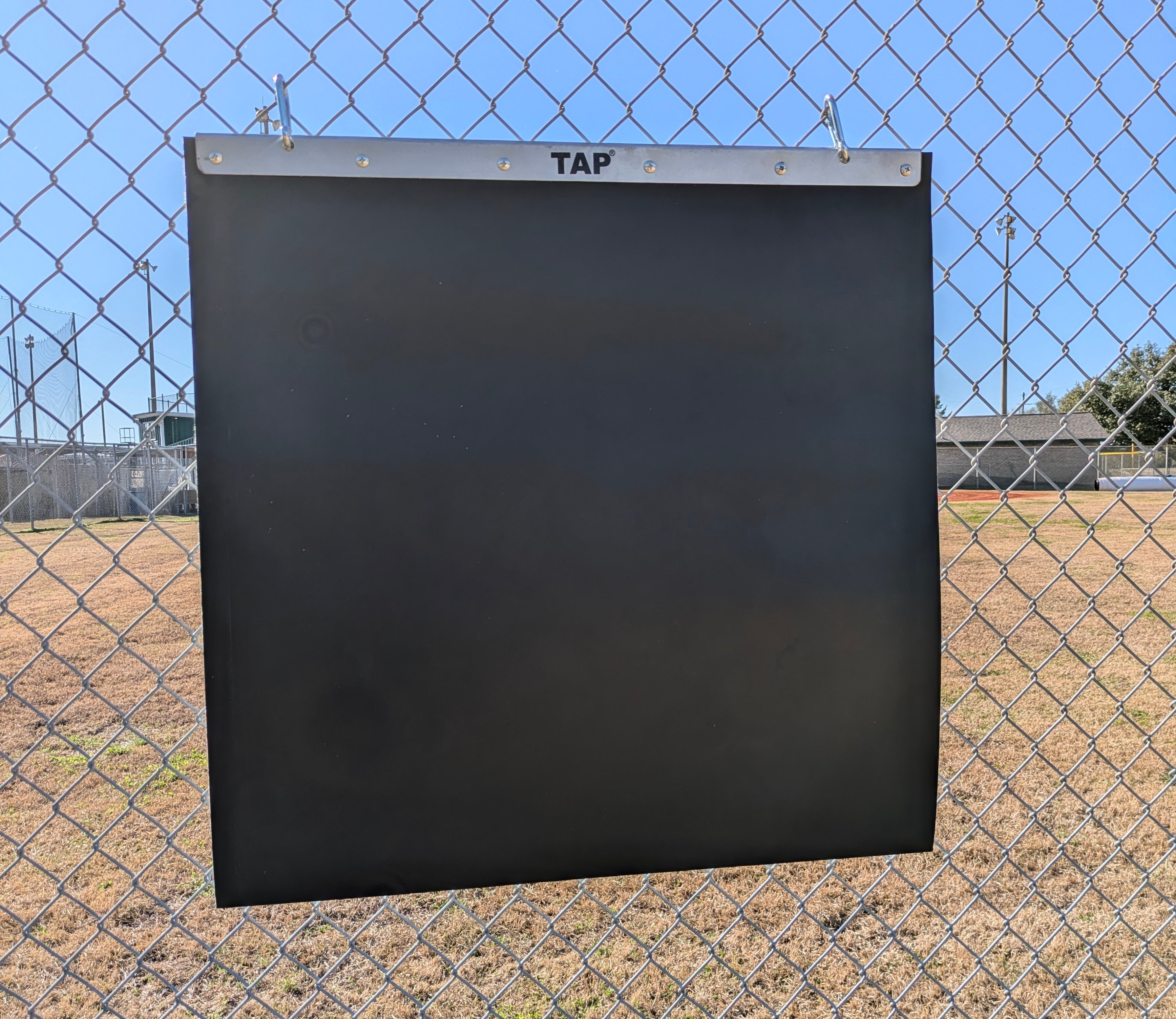 TAP® Portable Plyo Mat is hung from a chain link fence using the hooks provided with the product for which it is ready to have weighted balls or baseballs being thrown at it