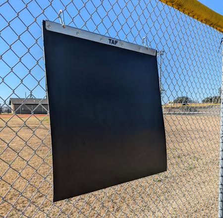The Portable Plyo Mat is hanging from a chain link fence next to a baseball field