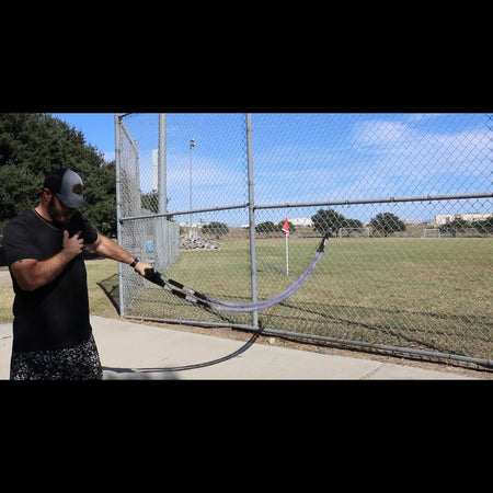 Athlete performing up down waves exercise with TAP Sheathed Safety Tubing anchored to a fence