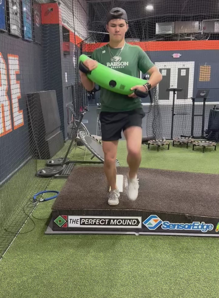 Pitcher training on a mound with the KHAOS Bulgarian Water Bag, utilizing dynamic water perturbations to stabilize the kinetic chain and maximize power transfer through the throwing arm.