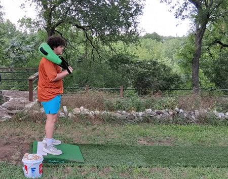 Young pitcher wearing a Bulgarian Water Bag over his shoulders, preparing to execute a pitching delivery while utilizing shifting water resistance to enhance core stability, strength, and movement control.