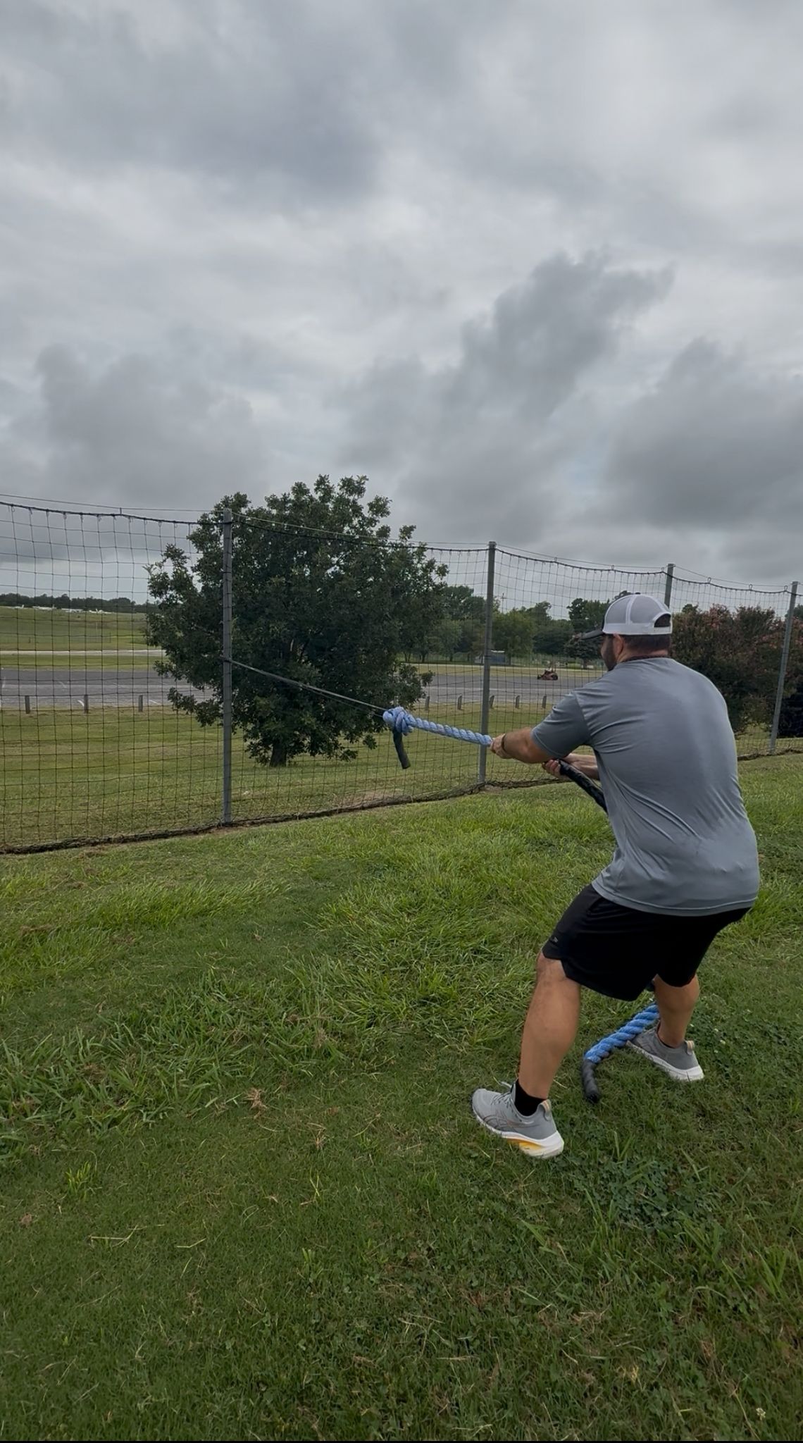 An athlete demonstrates hand-over-hand rope pulls, utilizing a thick rope connected to a giant flat resistance band, which provides dynamic tension for strength and grip training.