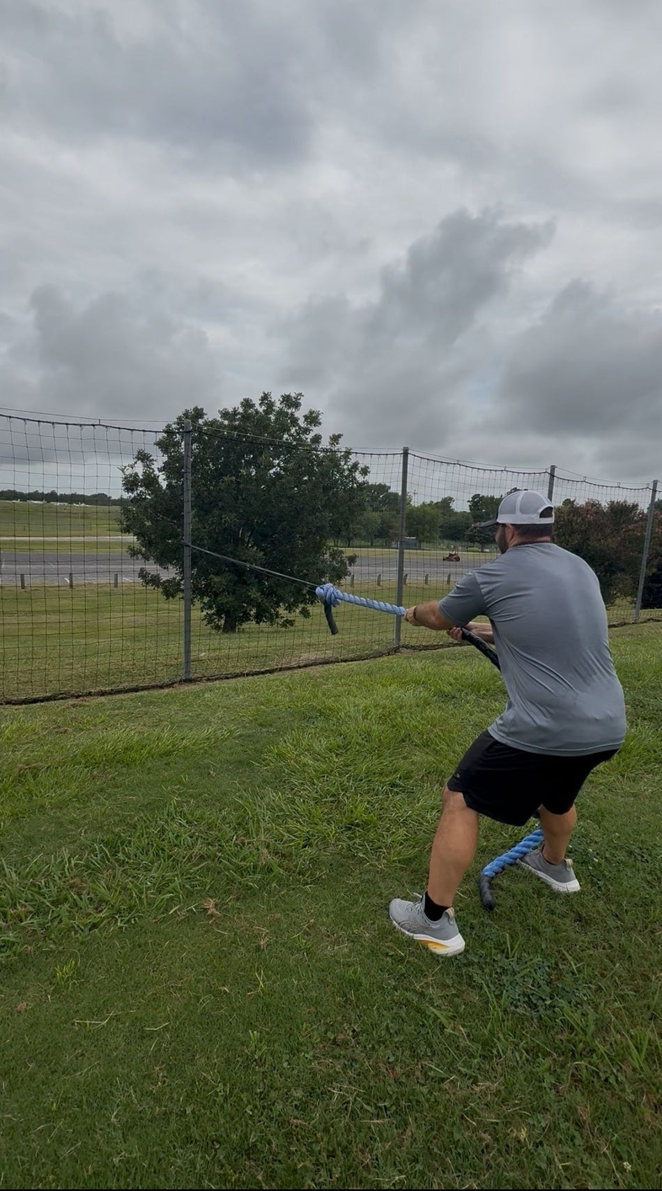 An athlete demonstrates hand-over-hand rope pulls, utilizing a thick rope connected to a giant flat resistance band, which provides dynamic tension for strength and grip training.