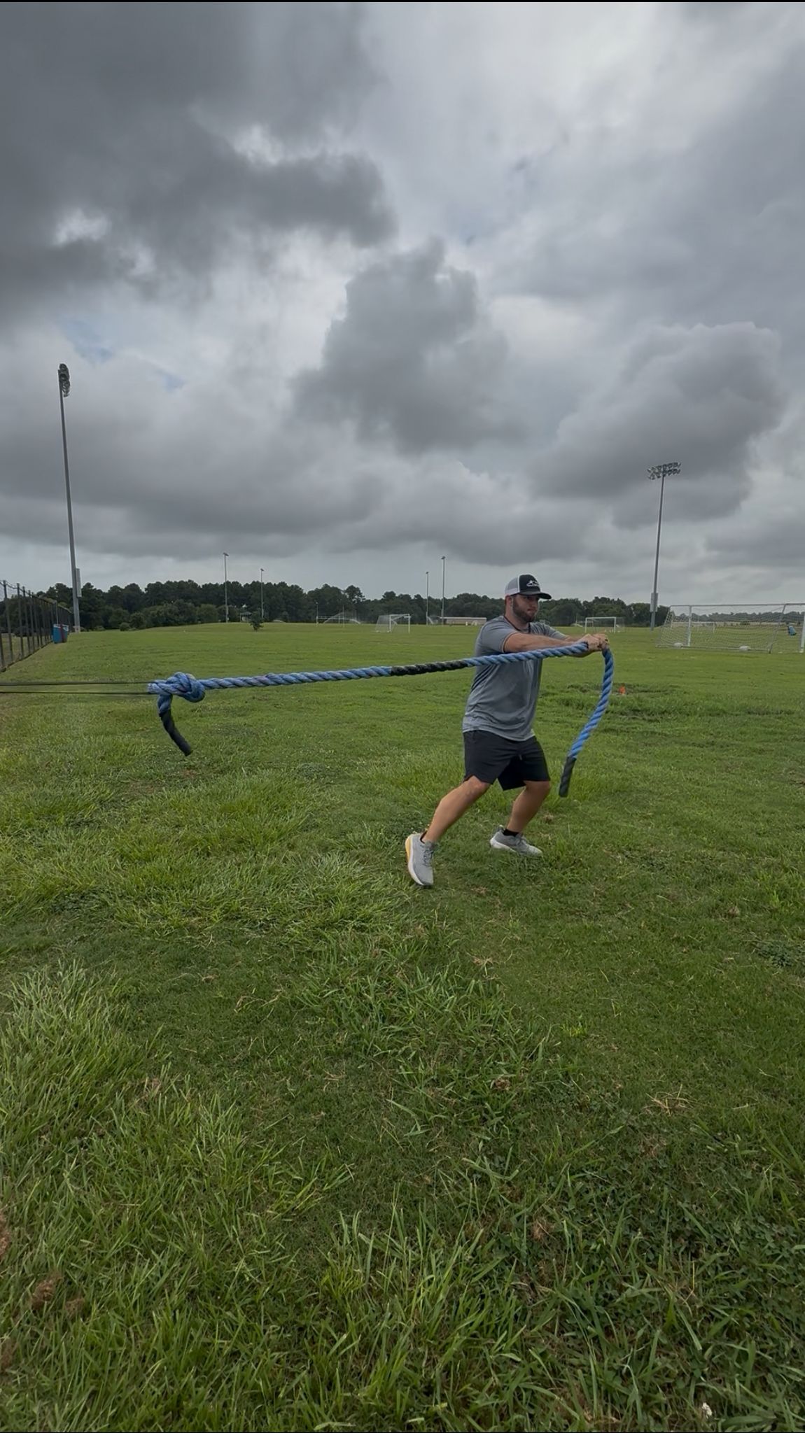 Action shot of an athlete bracing their core, holding a rope outwards as it pulls against a giant flat band, demonstrating an exercise for rotational and core stability.