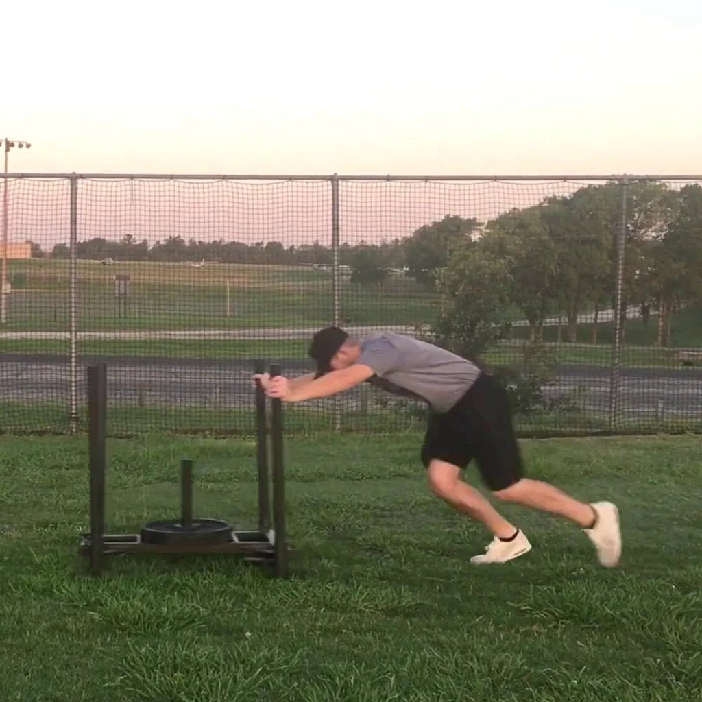 Athlete pushing a KHAOS® Wheelbarrow Sled without a wheel, performing a strength and endurance workout on a training surface, emphasizing full-body power and resistance-based conditioning.