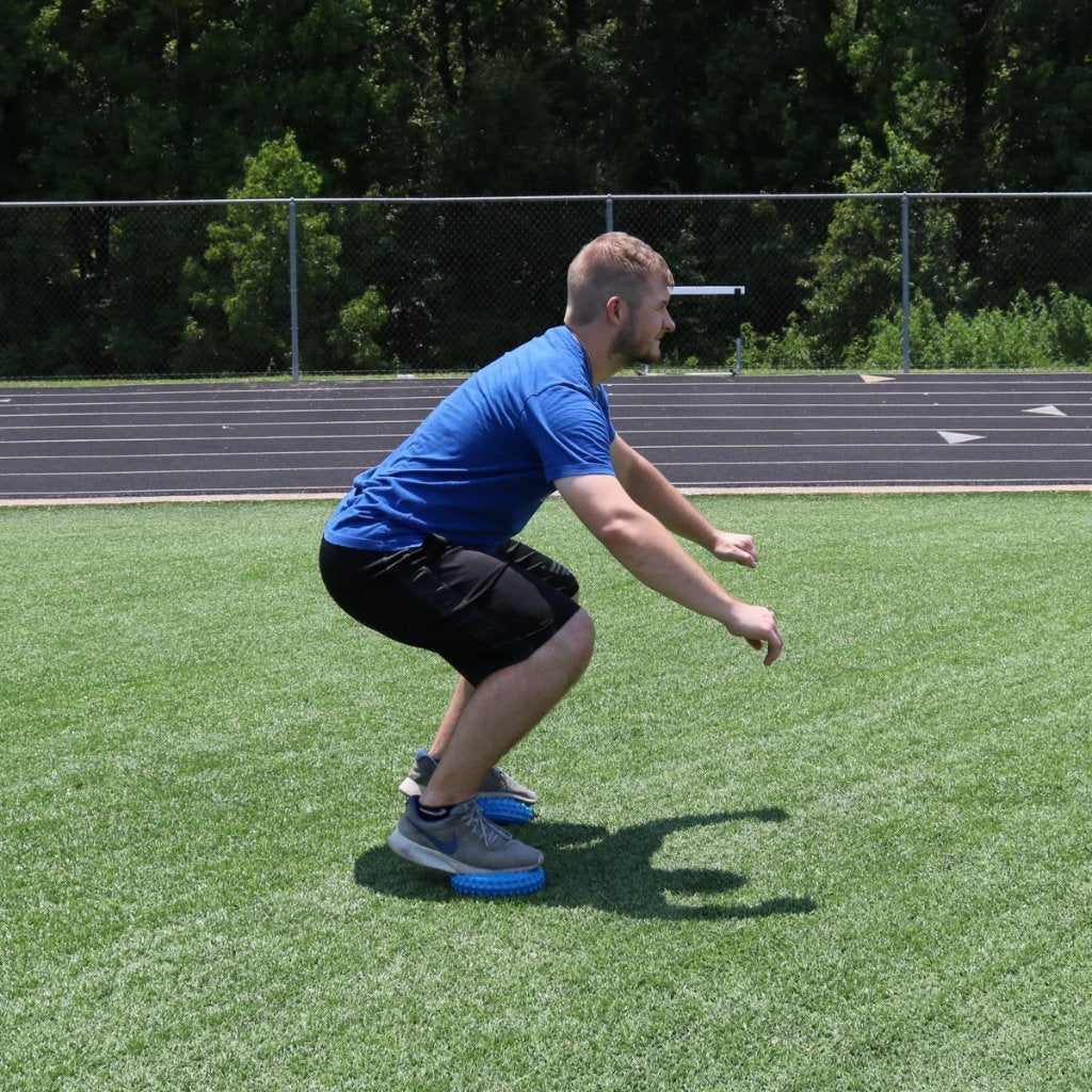 Balance Pod being used by both feet being stepped on while performing a squat to add an extra layer of difficulty.
